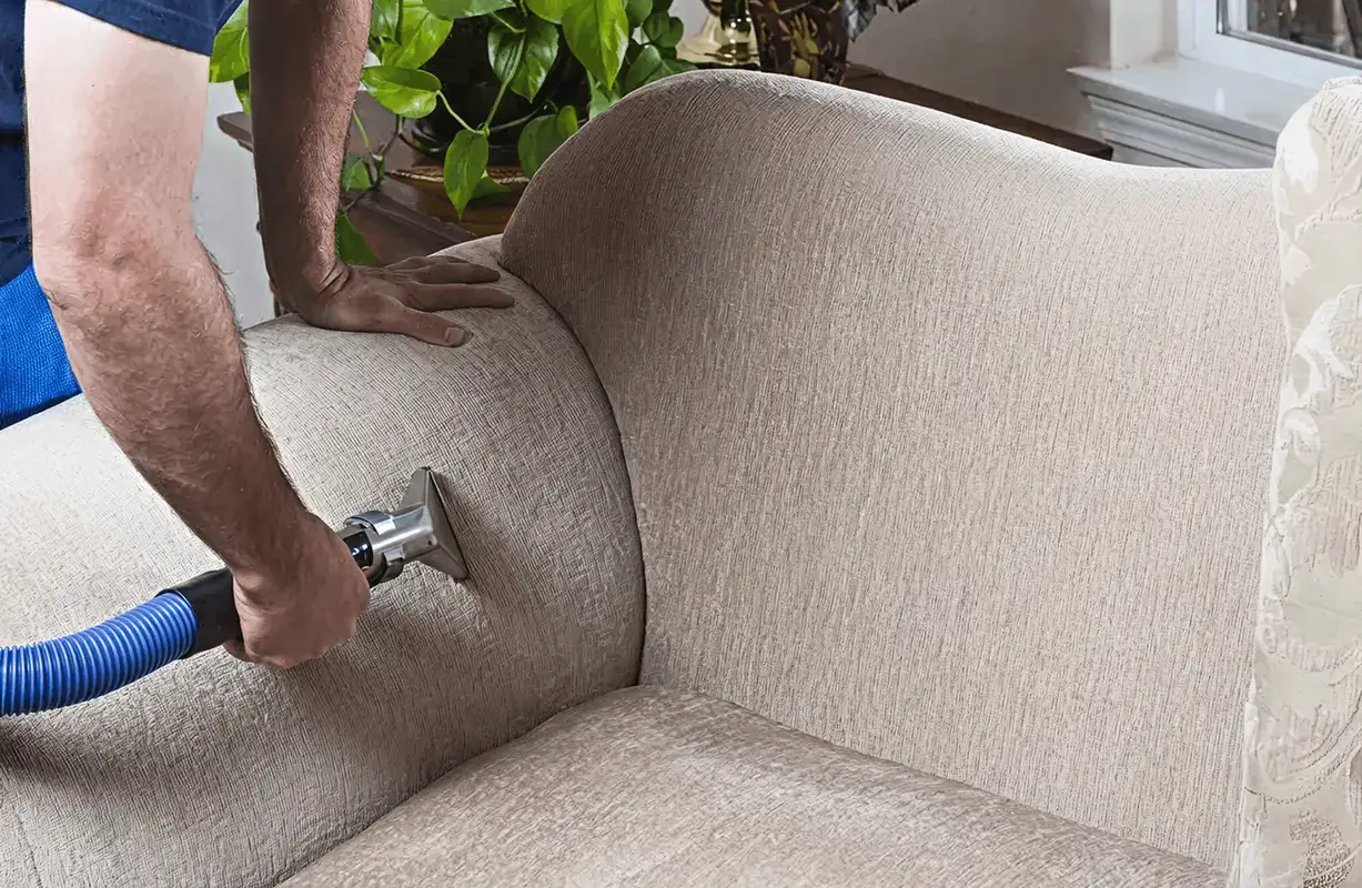 Professional upholstery cleaner deep-cleaning a fabric sofa with a handheld extraction tool and hose, Staten Island, NY.